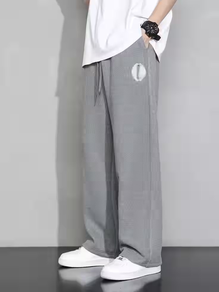 Grey wide-leg pants with a white cowrie emblem on the thigh